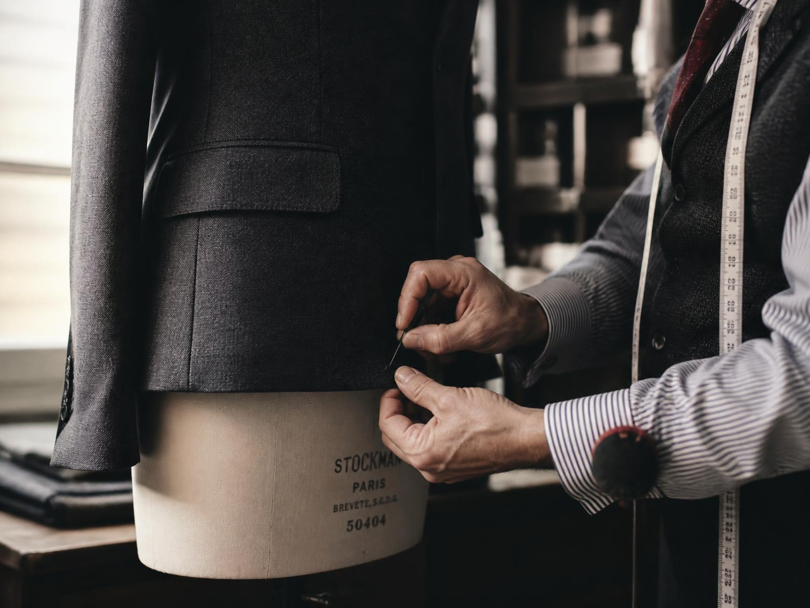 A tailor pinning the hem of a wool jacket on a dress form